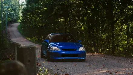 A vibrant blue Honda Civic parked on a scenic forest road, showcasing its JDM style against a backdrop of lush greenery, designed as a 4K Ultra HD desktop wallpaper.
