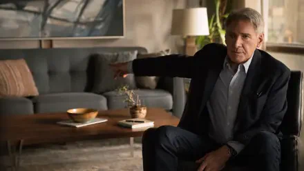 A scene from the TV show Shrinking, featuring a character portrayed by Harrison Ford. He gestures from a comfortable living space with modern decor.