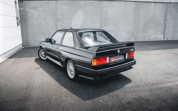 HD desktop wallpaper featuring a sleek black BMW E30 M3 parked against a concrete wall, showcasing the classic design of this iconic BMW vehicle.