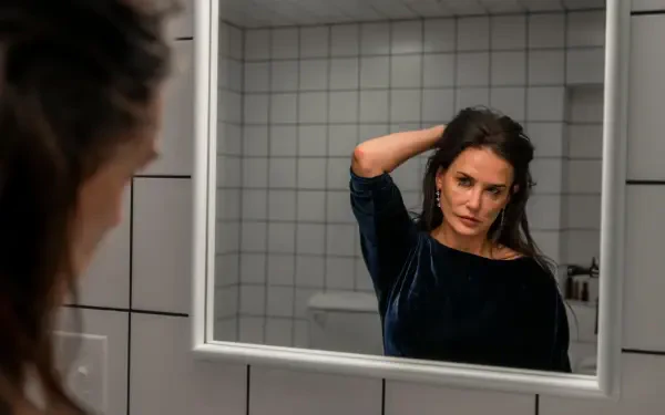 Demi Moore gazes thoughtfully at her reflection in a mirror, captured in a scene from the movie The Substance. This high-definition image serves as a striking desktop wallpaper.