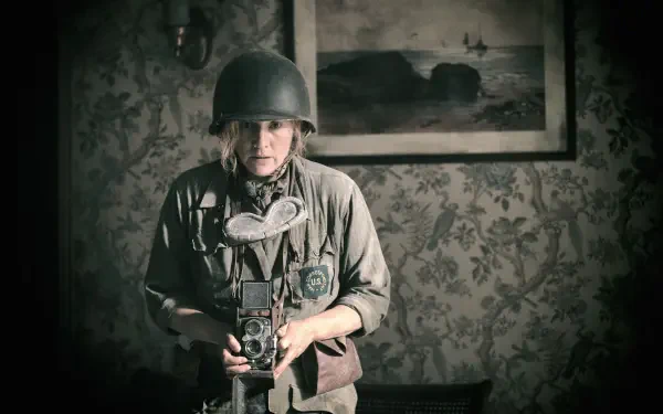 A scene from the movie Lee (2023) featuring Kate Winslet, depicting a soldier in a vintage setting, holding a camera amidst a richly patterned background.