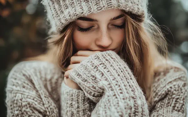 A woman in a cozy sweater and knit hat gently hugs her hands, embodying warmth and serenity. This 4K Ultra HD image serves as an inviting desktop wallpaper and background.