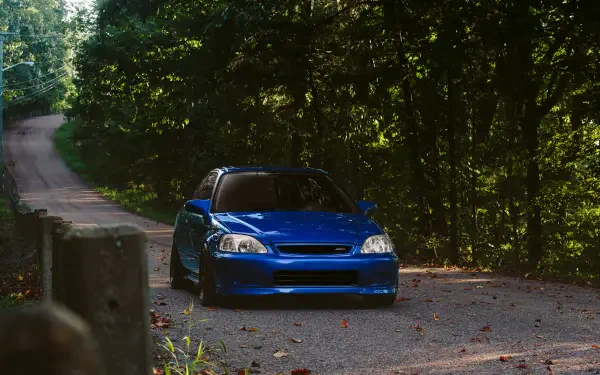 A vibrant blue Honda Civic parked on a scenic forest road, showcasing its JDM style against a backdrop of lush greenery, designed as a 4K Ultra HD desktop wallpaper.