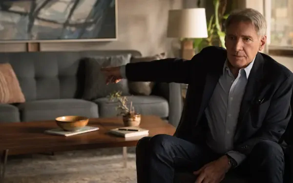 A scene from the TV show Shrinking, featuring a character portrayed by Harrison Ford. He gestures from a comfortable living space with modern decor.