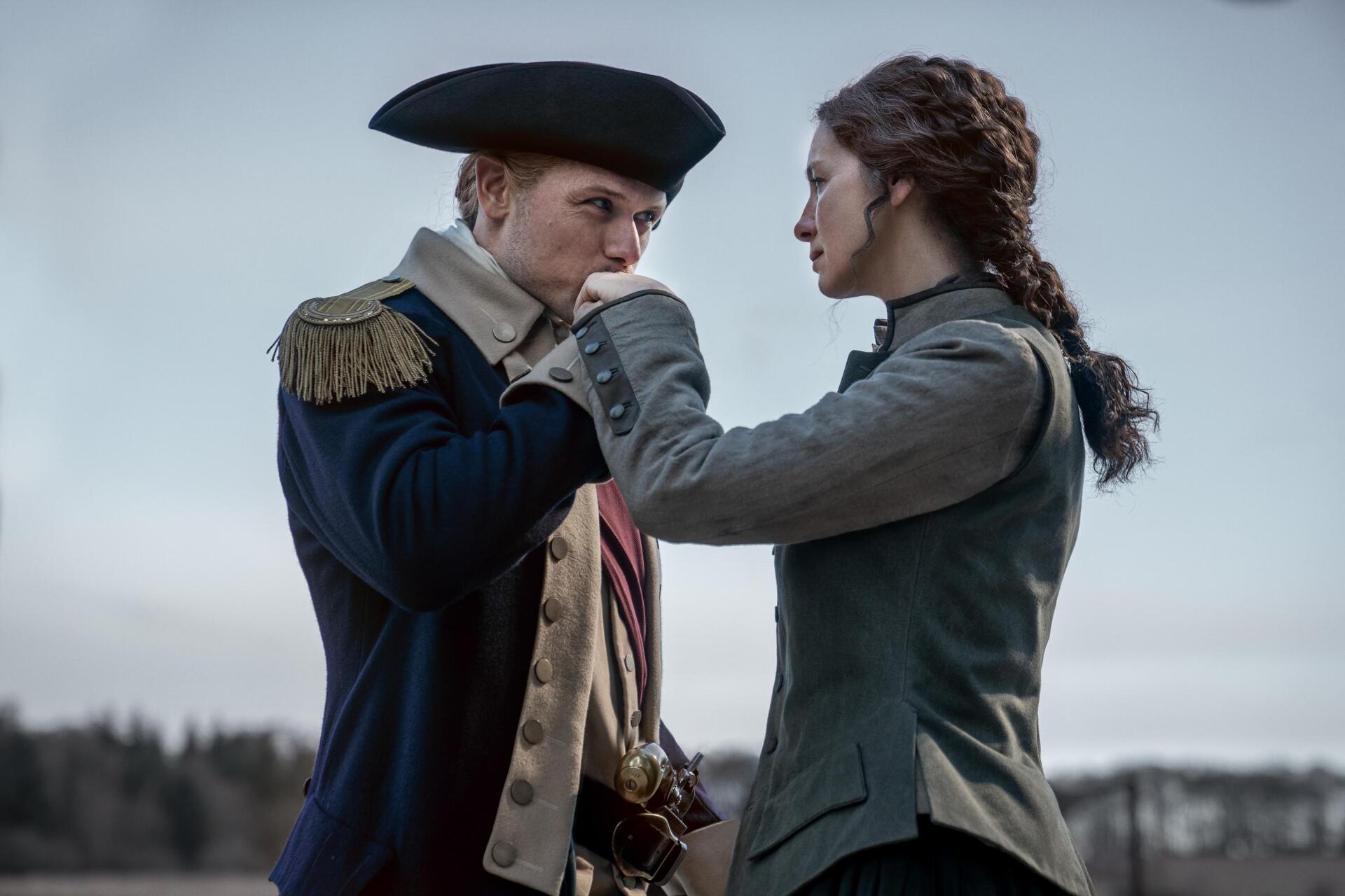 A dramatic moment from the TV show Outlander, featuring two characters in historical attire, capturing a sense of tension and connection against a muted outdoor backdrop.