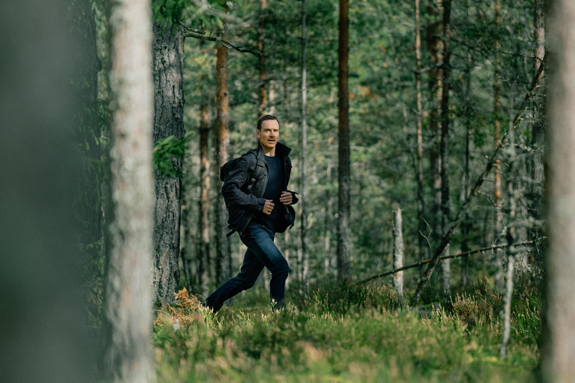 A scene from the TV show The Agency, featuring Michael Fassbender running through a lush green forest, captured in stunning 4K Ultra HD.