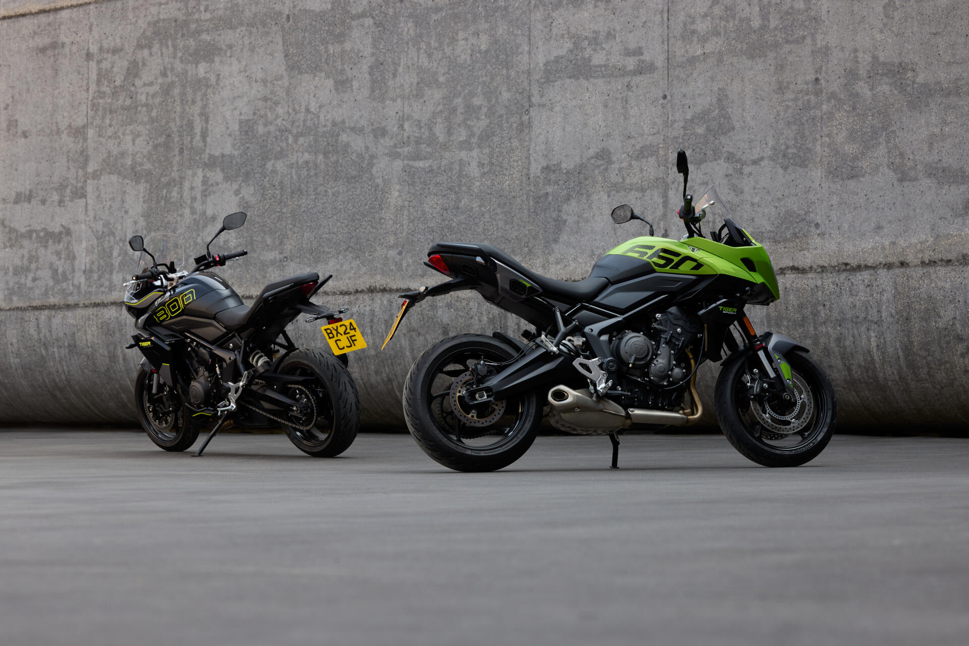 A striking 4K Ultra HD wallpaper featuring two Triumph motorcycles, the Tiger Sport 660 and another model, set against a minimalist concrete backdrop.