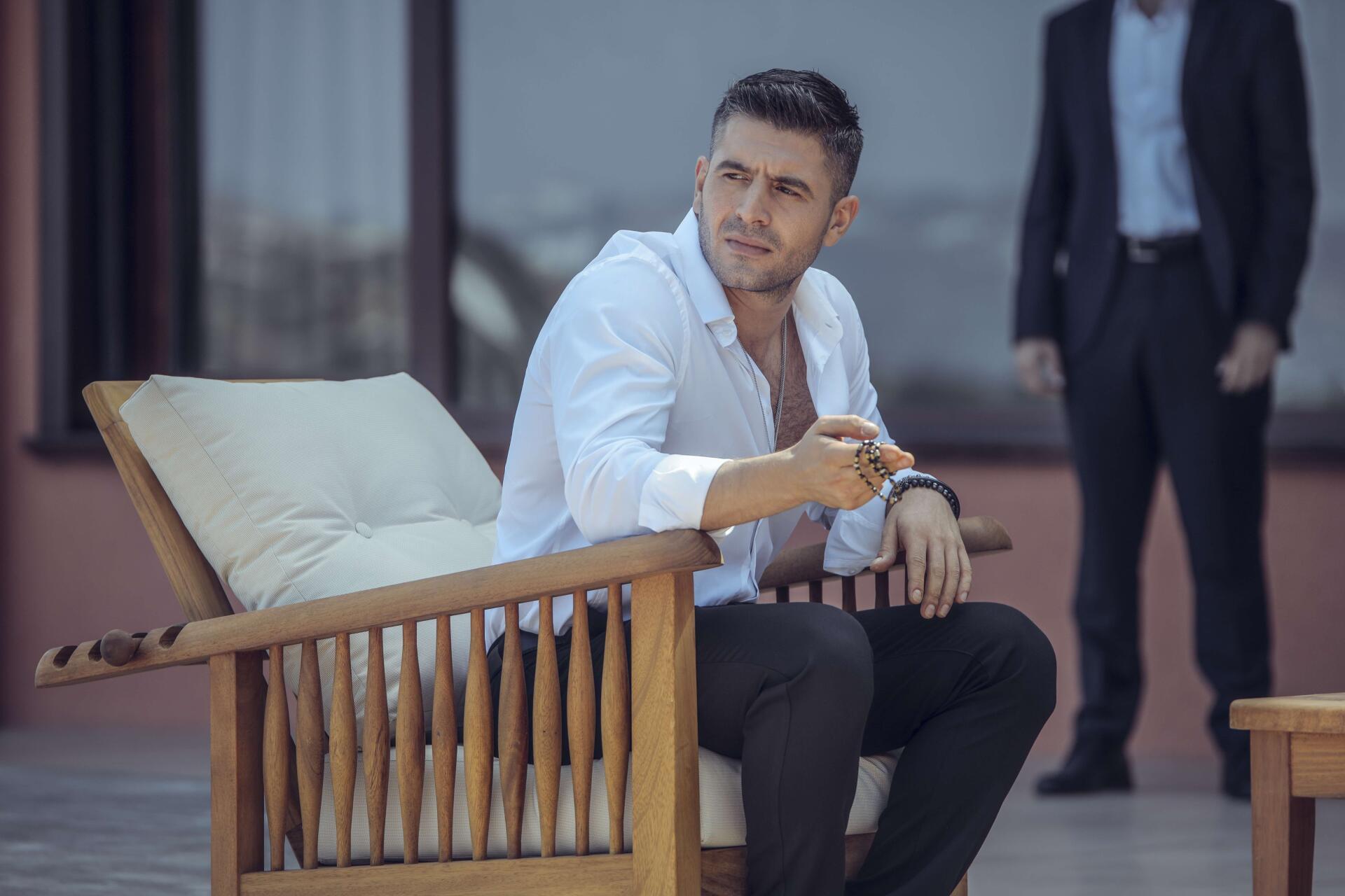 A scene from the TV show The Pit, featuring a man in a white shirt seated on a wooden chair, with a serious expression, complemented by a stylish background. 4K Ultra HD wallpaper.