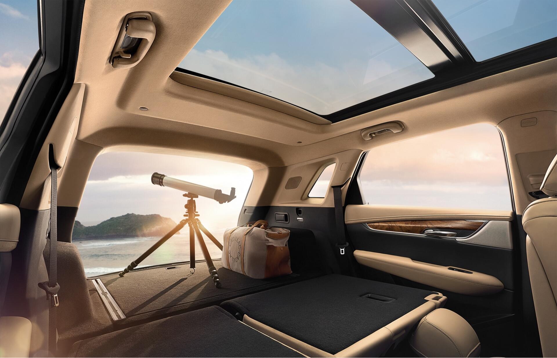 Interior of a Cadillac XT5 showcasing a spacious design with a panoramic sunroof, featuring a telescope and luggage, set against a scenic backdrop. HD PC desktop wallpaper.