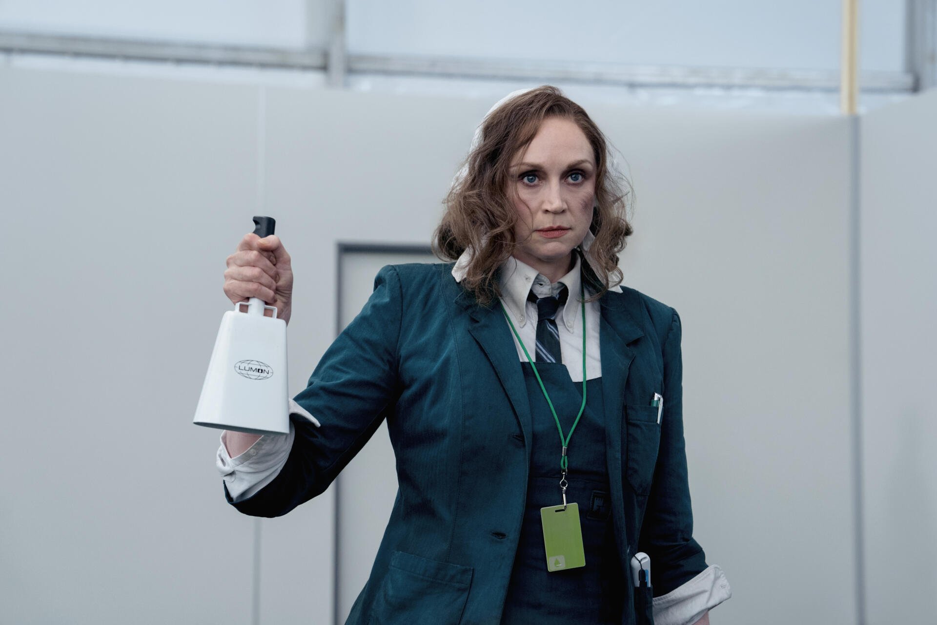 A scene from the TV show Severance, featuring Gwendoline Christie holding a bell, dressed in a dark green suit, set in a minimalist workspace. 4K Ultra HD wallpaper.