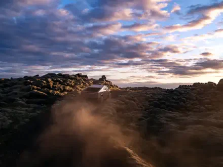A Tesla Cybertruck driving through rugged terrain under a dramatic sky, capturing the vehicle's off-road capability in stunning 4K Ultra HD.