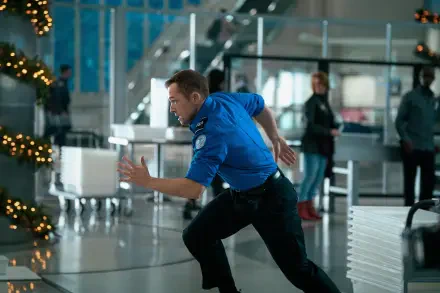 A security guard in a blue uniform runs through an airport terminal, capturing the action and energy of the movie Carry On (2024). 4K Ultra HD desktop wallpaper.