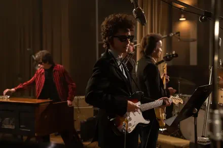 A scene from the movie A Complete Unknown, showcasing Timothée Chalamet performing with a guitar, surrounded by musicians in a vintage studio setting. 8K Ultra HD wallpaper.