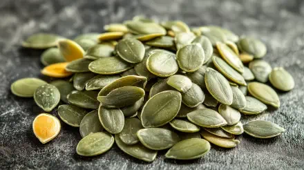 A close-up of a pile of pumpkin seeds on a textured surface, featuring their rich green color. This vibrant image serves as a stunning 4K Ultra HD desktop wallpaper.