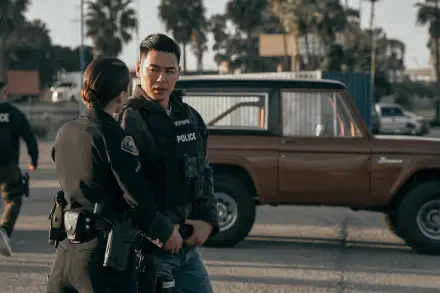 A scene from the TV show On Call (2025) featuring two police officers engaged in conversation, with a vintage brown vehicle and palm trees in the background. 4K Ultra HD wallpaper.