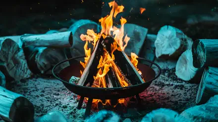 A cozy fire pit with vibrant flames, surrounded by logs and glowing embers, showcased in stunning 4K Ultra HD, perfect for a desktop background or wallpaper.