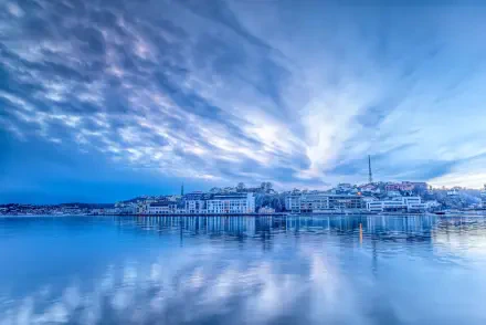 5K Ultra HD PC desktop wallpaper and background of a serene coastal city skyline at dawn, glassy water reflecting waterfront buildings beneath a dramatic blue sky.