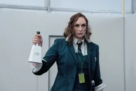 A scene from the TV show Severance, featuring Gwendoline Christie holding a bell, dressed in a dark green suit, set in a minimalist workspace. 4K Ultra HD wallpaper.
