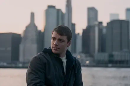 Gabriel Basso in a scene from the TV show The Night Agent, seated against a backdrop of a city skyline during twilight, creating a dramatic and engaging atmosphere.
