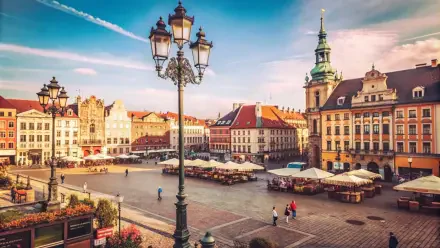 5K Ultra HD PC desktop wallpaper and background: sunlit historic city square with an ornate lamppost, outdoor market stalls, colorful townhouses and a church spire beneath a blue sky.