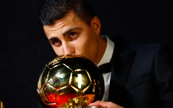 Rodri Hernández, dressed in a tuxedo, kisses the Ballon d'Or trophy, showcasing his triumph in soccer. This HD wallpaper captures a moment of celebration and achievement.