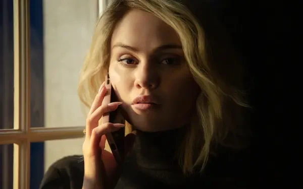 A captivating 4K Ultra HD wallpaper featuring Emilia Pérez, portrayed by Selena Gomez, deeply engaged in a phone conversation by a window with dramatic lighting.