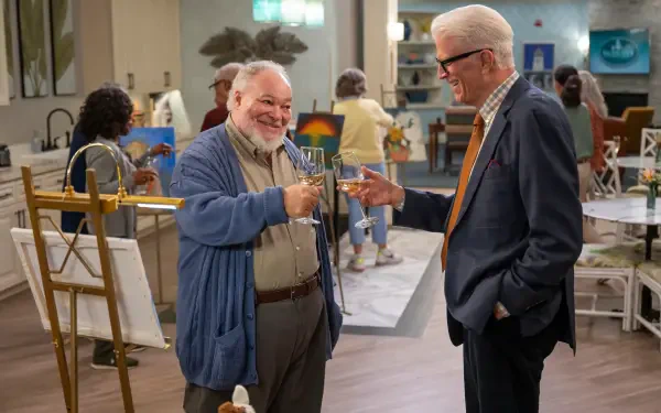A scene from the TV show A Man on the Inside featuring Ted Danson and Stephen McKinley Henderson sharing a toast, set in a vibrant community space.