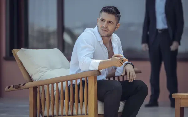 A scene from the TV show The Pit, featuring a man in a white shirt seated on a wooden chair, with a serious expression, complemented by a stylish background. 4K Ultra HD wallpaper.