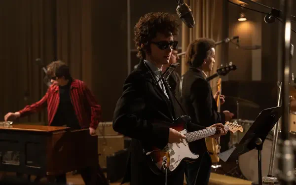 A scene from the movie A Complete Unknown, showcasing Timothée Chalamet performing with a guitar, surrounded by musicians in a vintage studio setting. 8K Ultra HD wallpaper.