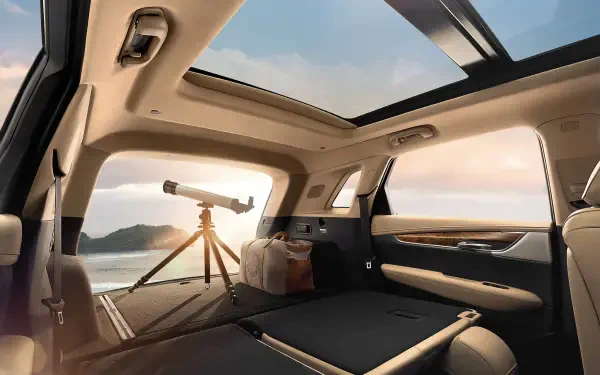 Interior of a Cadillac XT5 showcasing a spacious design with a panoramic sunroof, featuring a telescope and luggage, set against a scenic backdrop. HD PC desktop wallpaper.