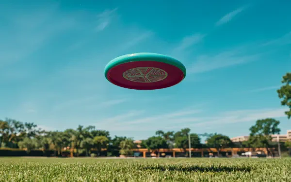 A colorful frisbee hovers above lush green grass under a clear blue sky, featured as a vibrant 4K Ultra HD desktop wallpaper and background.