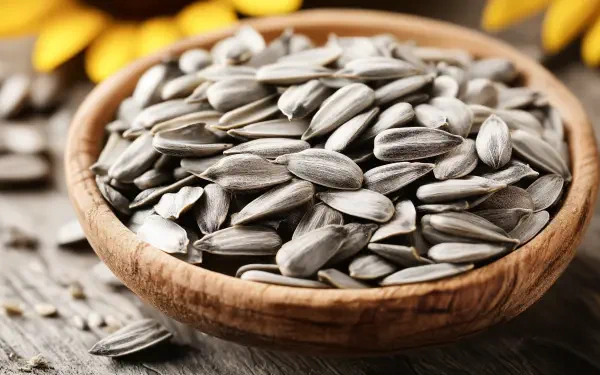 A close-up of a wooden bowl filled with sunflower seeds, surrounded by sunflower petals, captured in rich detail for a 4K Ultra HD desktop wallpaper.