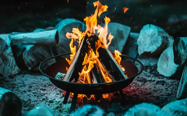 A cozy fire pit with vibrant flames, surrounded by logs and glowing embers, showcased in stunning 4K Ultra HD, perfect for a desktop background or wallpaper.
