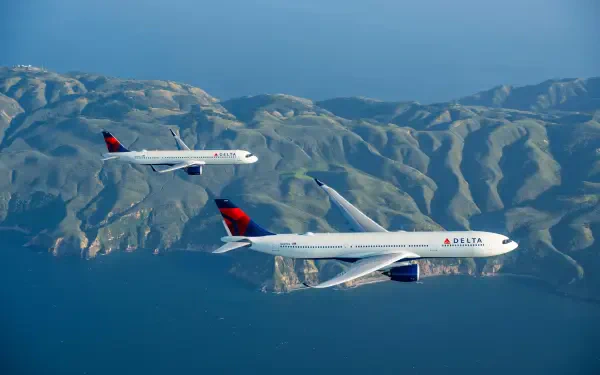 Two Delta Air Lines airplanes soar over a stunning landscape, showcasing mountains and ocean in a vibrant, 4K Ultra HD desktop wallpaper.