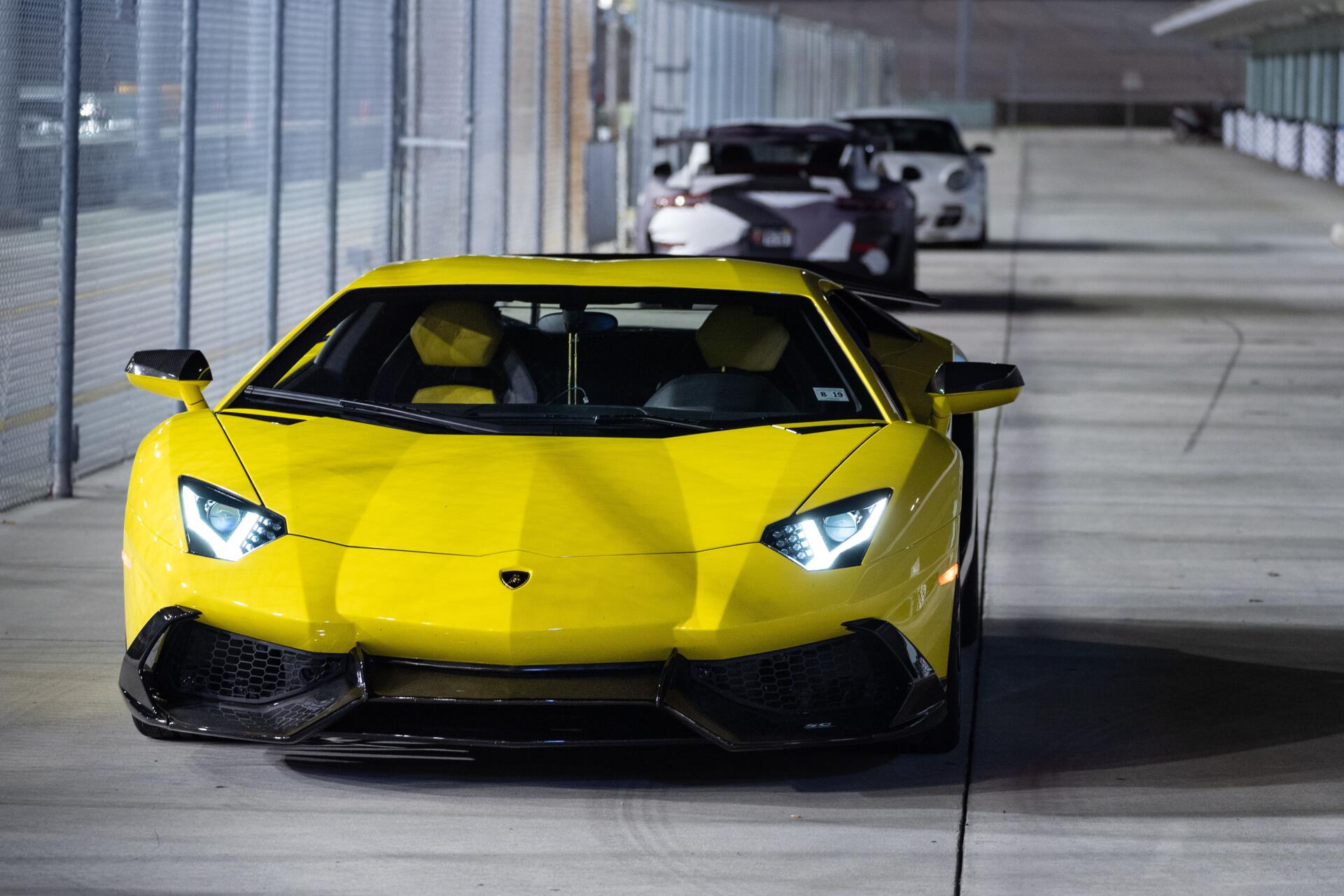 Front view of a yellow Lamborghini in a lit tunnel, high-detail 5K Ultra HD PC desktop wallpaper showing headlights on and a second car trailing behind.