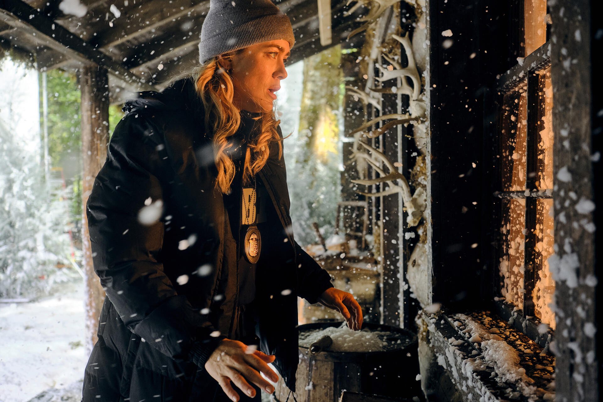 Melissa Roxburgh in a snowy scene from the TV show The Hunting Party (2025), wearing a beanie and coat, engaging with a cozy fireplace backdrop. HD wallpaper for desktop backgrounds.