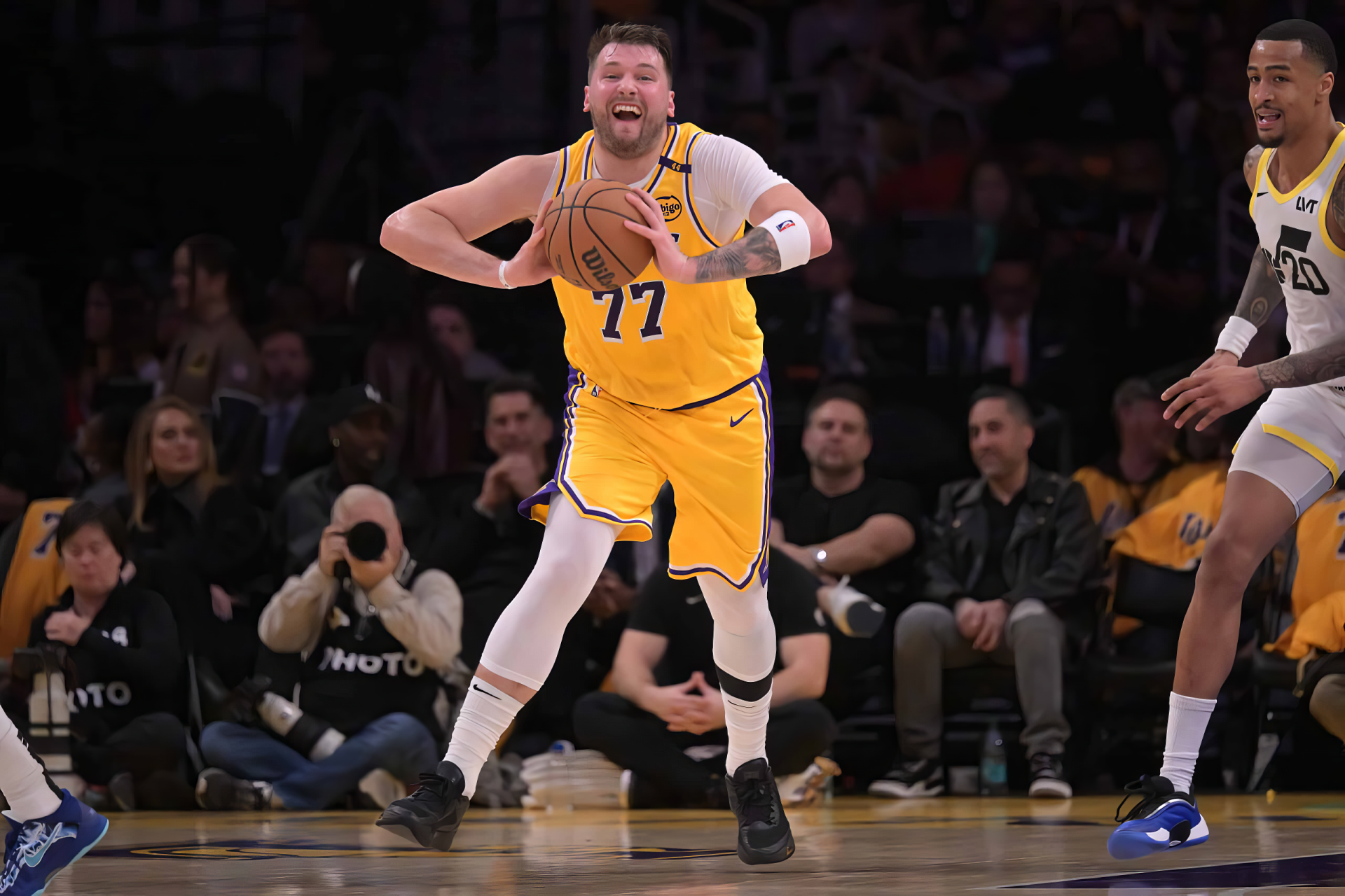 An action-packed image of Luka Dončić wearing a Los Angeles Lakers jersey, dribbling a basketball during an NBA game, with fans and teammates in the background.