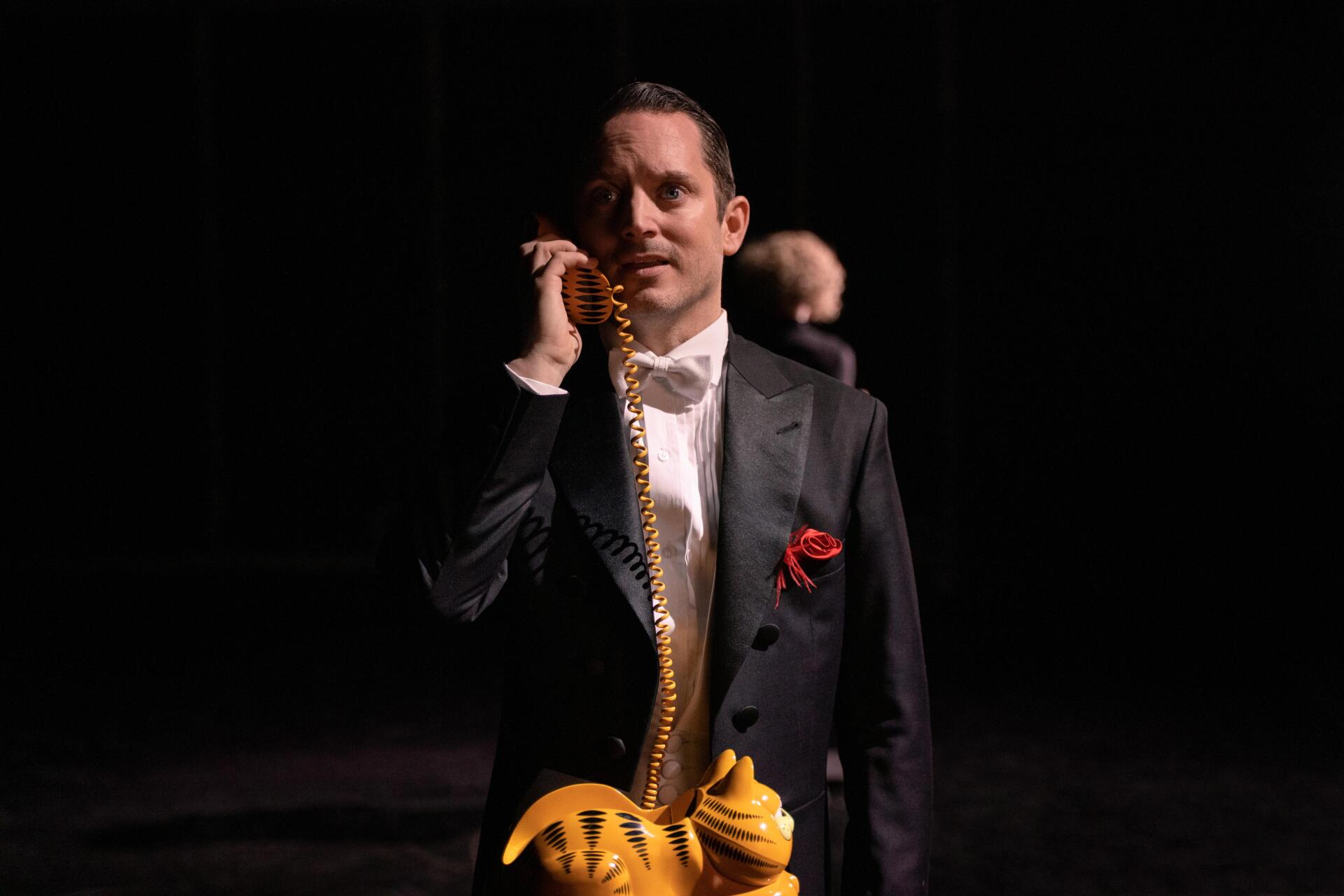 A scene from the TV show Yellowjackets, featuring Elijah Wood in a tuxedo, holding a whimsical phone. The image is a striking 4K Ultra HD wallpaper.