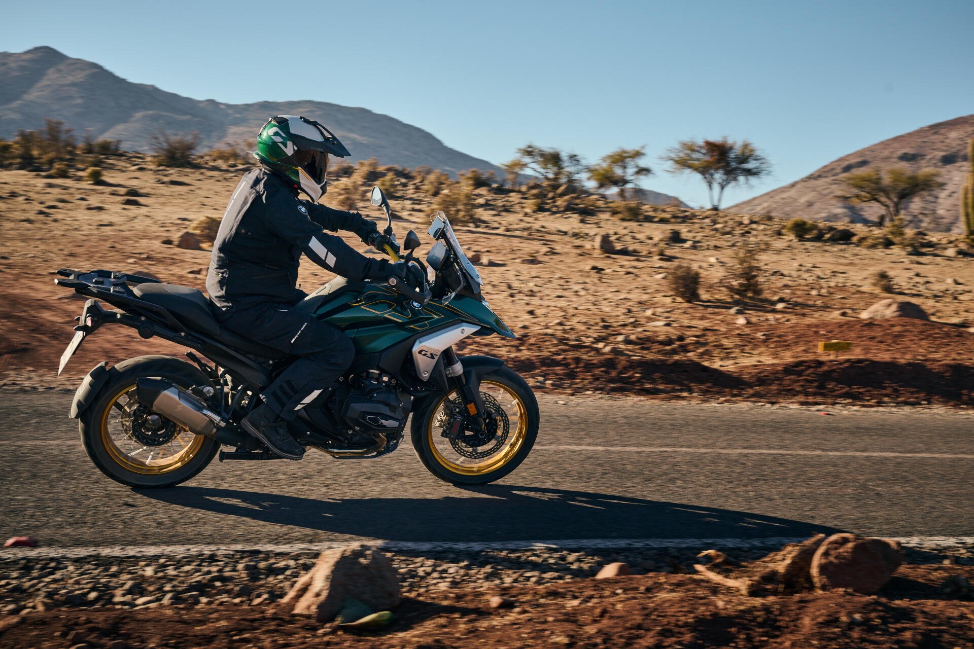 A BMW R1300GS motorcycle is riding along a desert road, with mountains in the background, captured in stunning 4K Ultra HD detail.