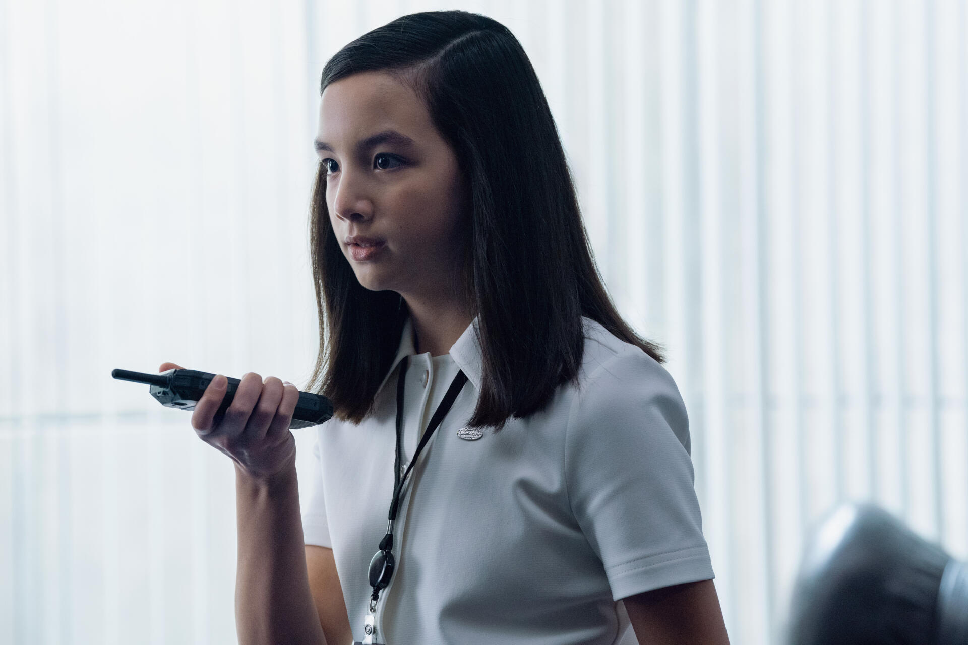 A young character from the TV show Severance, Sarah Bock, holds a device, engaged and thoughtful, set against a sleek, modern backdrop in this 4K Ultra HD wallpaper.