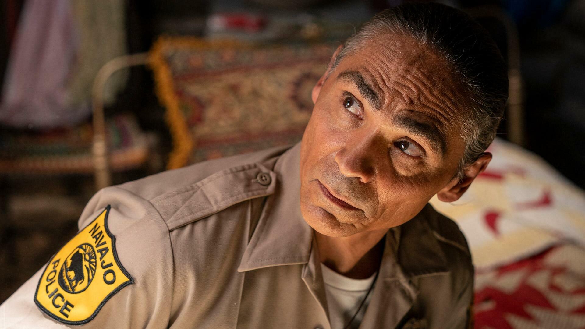 A captivating HD wallpaper from the TV show Dark Winds, featuring Zahn McClarnon in his character's uniform, gazing thoughtfully as he investigates a scene.