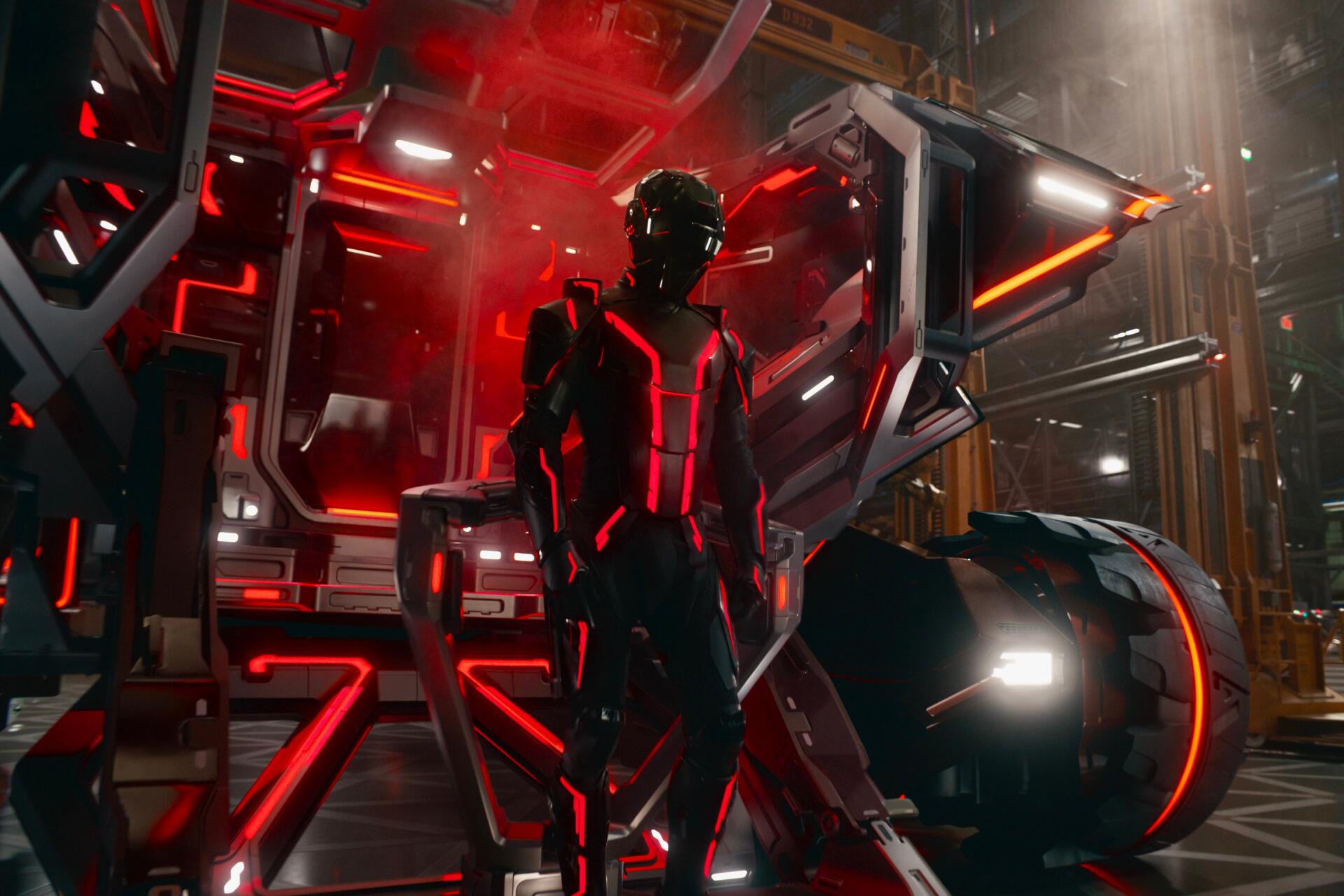 HD PC desktop wallpaper featuring a dark, futuristic figure with glowing red lines from the movie Tron: Ares, set in a high-tech industrial environment.