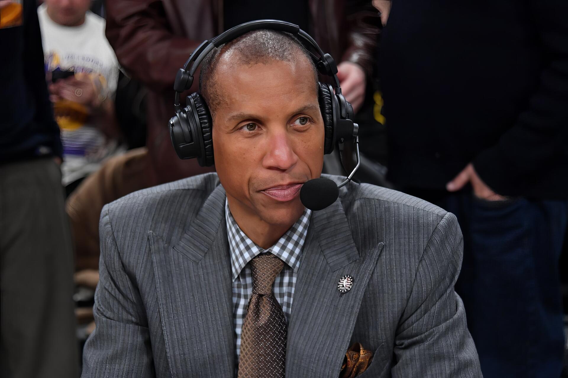 HD PC desktop wallpaper of Reggie Miller wearing a suit and headset, speaking during a broadcast with a blurred crowd in the background.