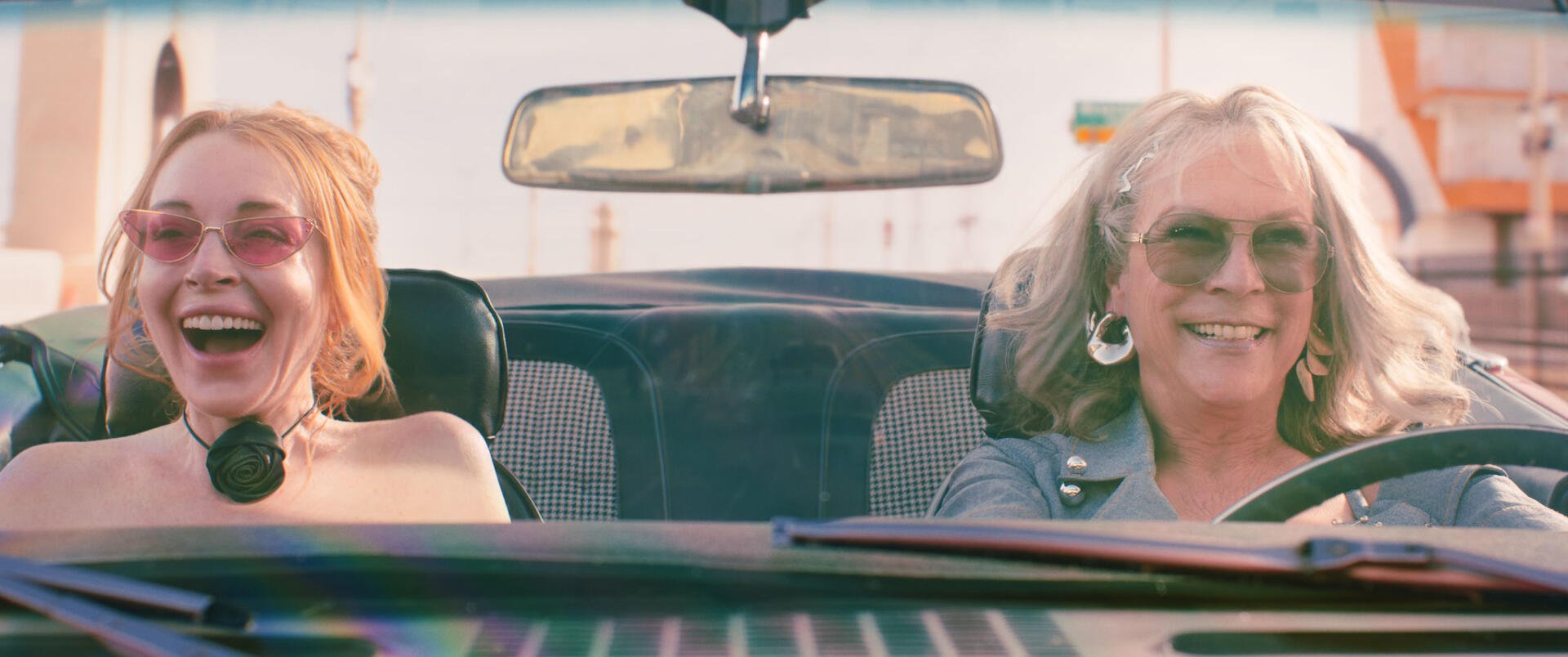 HD desktop wallpaper featuring Lindsay Lohan and Jamie Lee Curtis in a scene from the movie Freaky Friday, showing them smiling inside a car.