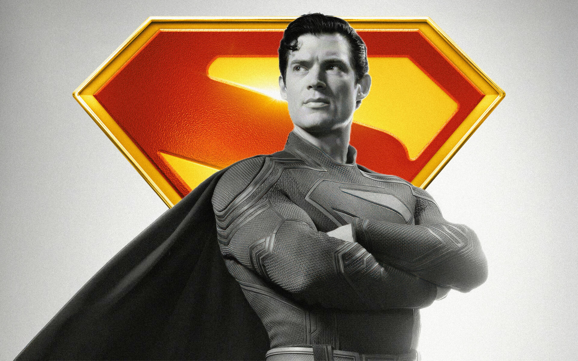 Superman (2025) grayscale chest-up portrait with arms crossed and cape before a vivid red-yellow S-shield — 4K Ultra HD PC desktop wallpaper/background.