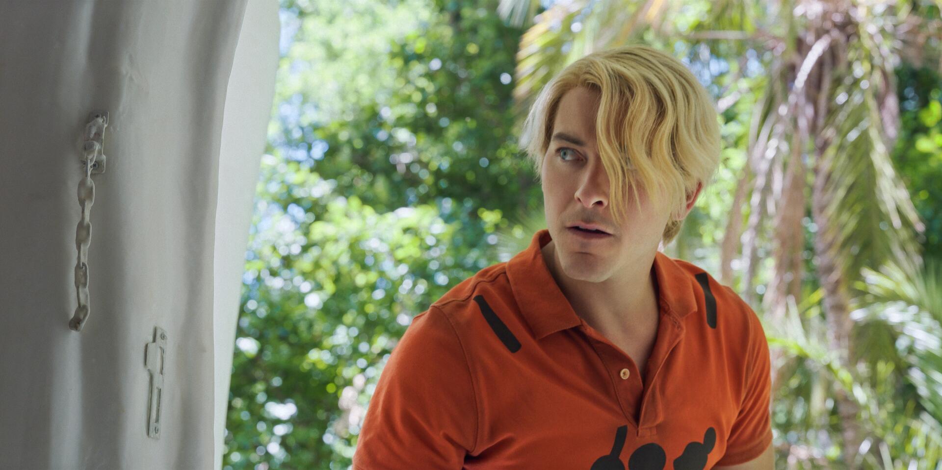 HD PC desktop wallpaper of Sanji from the One Piece live-action TV show: blond, side-swept hair and orange shirt peering from a doorway with sunlit tropical foliage.