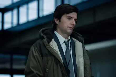 A 4K Ultra HD image from the TV show *Severance*, featuring Adam Scott in a contemplative moment, dressed in a coat and tie, set in a modern, industrial environment.