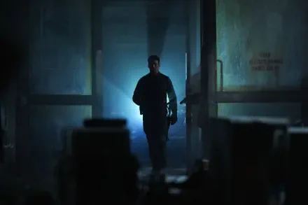 A dramatic scene from the movie The Gorge (2025) featuring Miles Teller. The image shows a lone figure walking through a dimly lit corridor, enhanced by striking light effects.