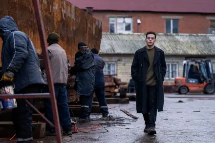 A scene from the movie The Amateur (2025) featuring Rami Malek, showcasing a gritty industrial setting with several workers and a lone figure walking amidst them. 8K Ultra HD quality.