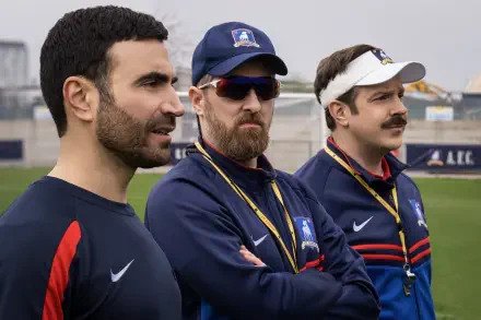 A scene from the TV show Ted Lasso, featuring Jason Sudeikis, Brendan Hunt, and Brett Goldstein as they observe a practice on the field, portrayed in vibrant 8K Ultra HD.